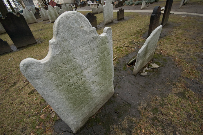 A thin old tombstone from the 18th century stands firm in a muddy church yard surrounded by the buildings which have cropped up in the intervening years.