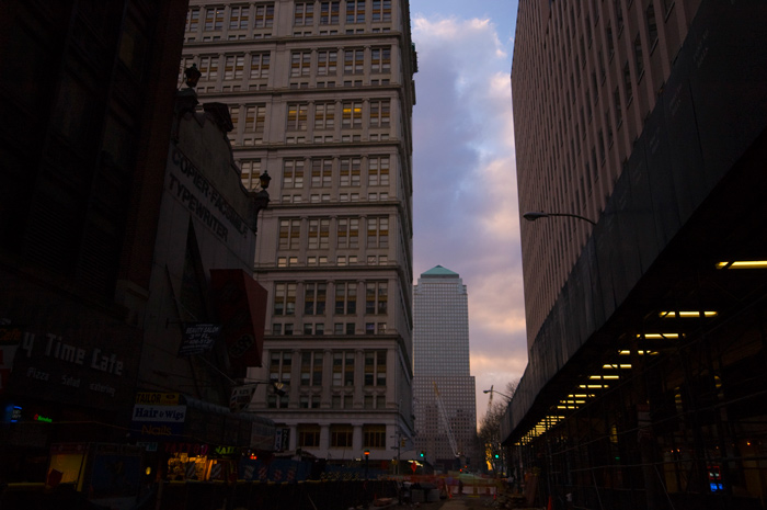 A tall building with a pyramid-shaped top peeks between foreground buildings as dusk falls.