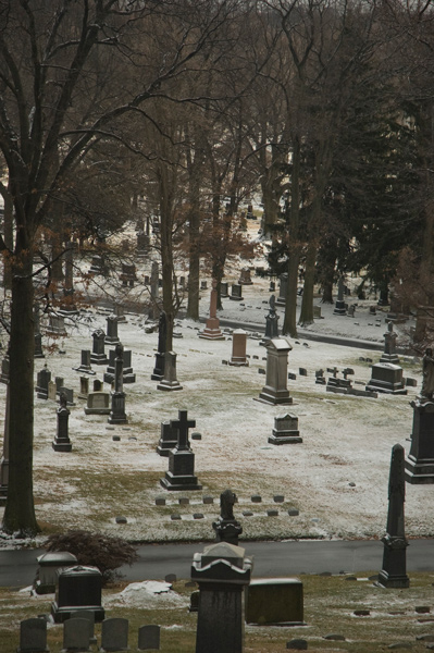 Below a rise, a lawn and tombstones have a dusting of snow.