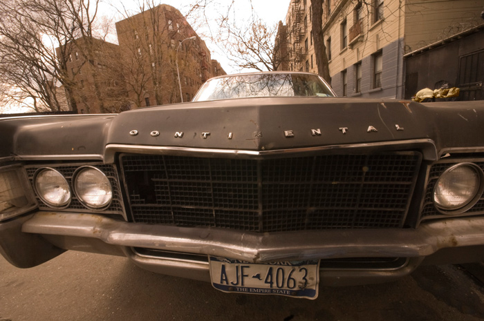 An old Lincoln Contintal has many dents and is missing letters from its name.