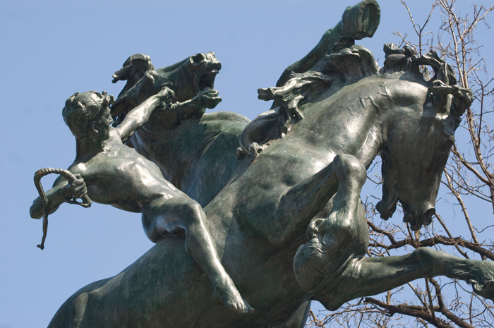 A statue shows a man taming horses.