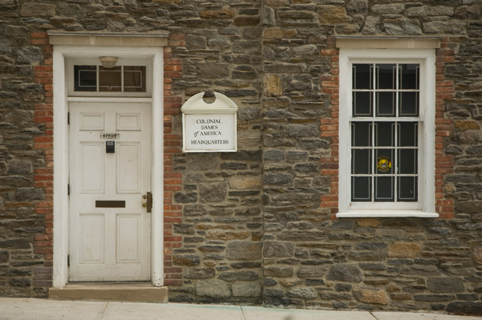 An old stone building with white wooden windows, shutters, and entrance serves as the headquarters of the Colonial Dames of America.