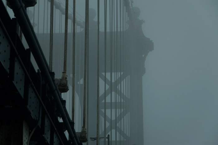 A photo of a portion of the Manhattan Bridge, showing supports and cables on a misty day.