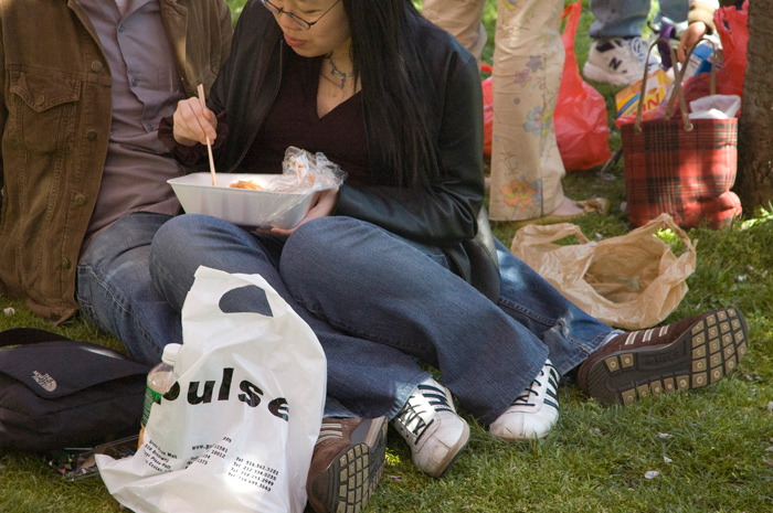 A woman uses chopsticks to eat Asian food at a Cherry Blossom festival.