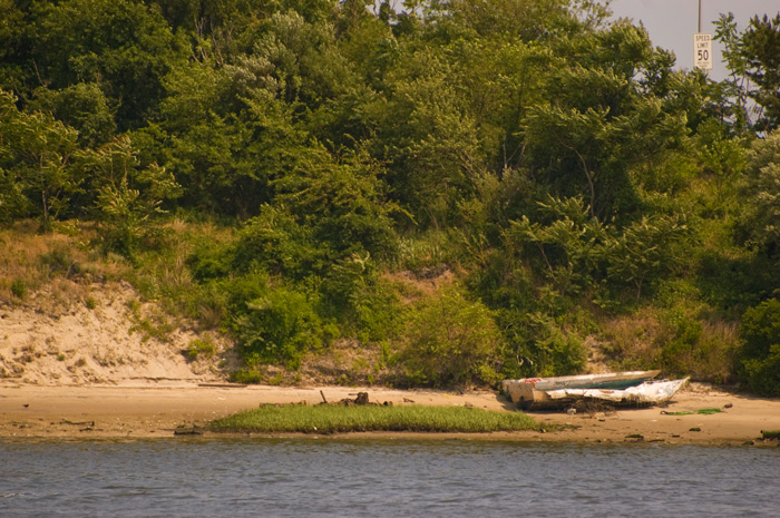 A small, worn out skiff lies on a shoreline, with no signs of attention in years.