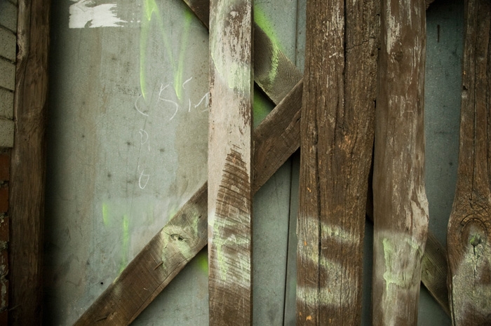 The words 'no trespassing' have been spraypainted on the weathered layers of a door and planks covering it.