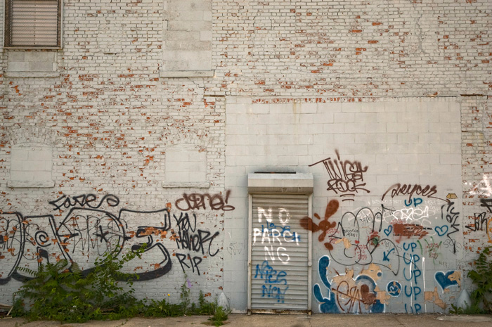 A brick wall is covered with graffiti for the first eight feet, but not above that height.