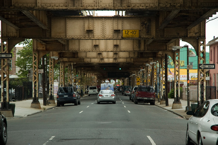 Cars fill a road heading into the distance, topped by elevated subway tracks.
