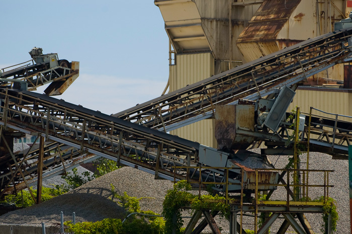 Several chutes and conveyor belts criscross at a cement factory, with a blue sky in the background.