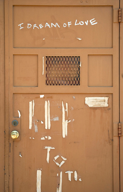 A bare, brown door has the words 'I Dream of Love' written on them in marker ink.