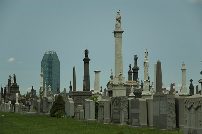 Several columns rise above graves, and Citibank's Queens tower is seen in the background.