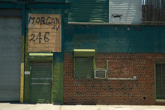 An industrial building's door has cinder blocks above it, on which the address has been crudely spray painted.