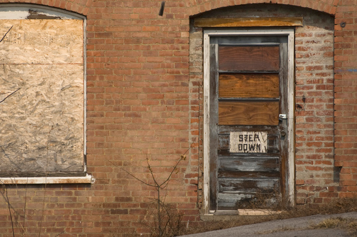 A sign on a wooden door, on an old brick building, warns to 'Step Down.'