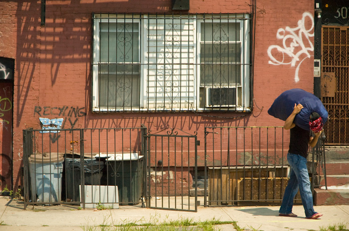 A man carrying a full laundry bag on his shoulder walks past an old building.