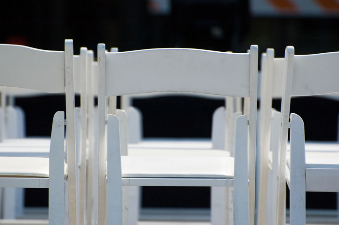 A row of empty white wooden folding chairs.