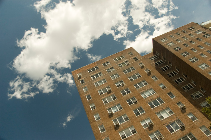 Two tall brick apartment buildings stand out against a blue sky with clouds.
