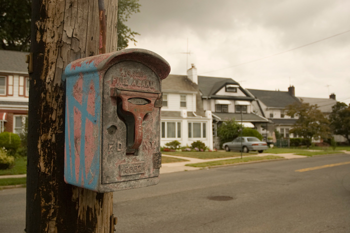 A weathered, graffiti'd fire call box on a telephone pole, on a residential block.