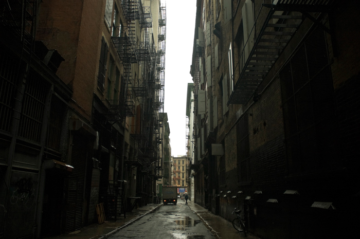 A sliver of light falls between a canyon formed by a dark alley.