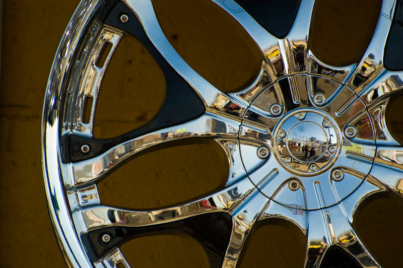 A showpiece chrome hubcap, hung on a drab wall, reflects blue sky and myriad surroundings.
