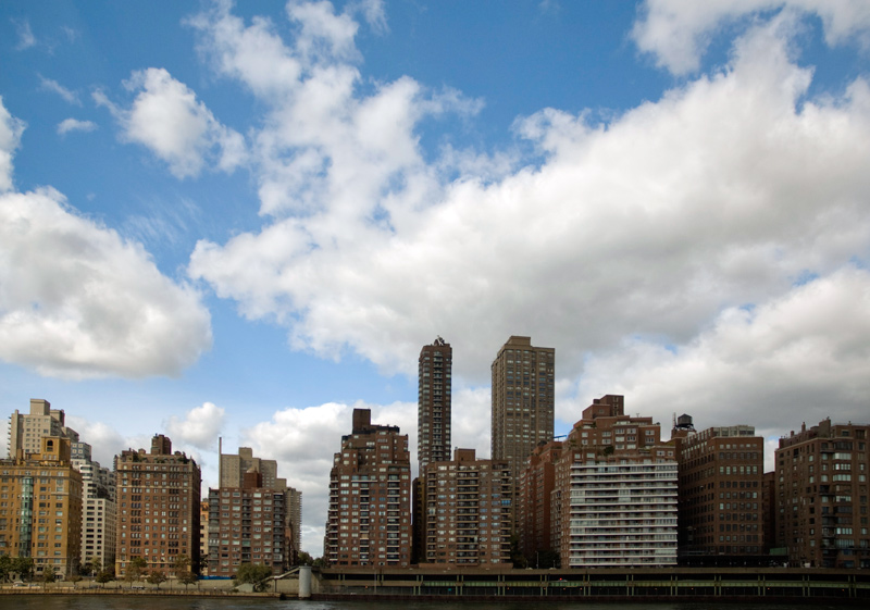 A line of tall apartment buildings, with a cloud-filled blue sky behind them.