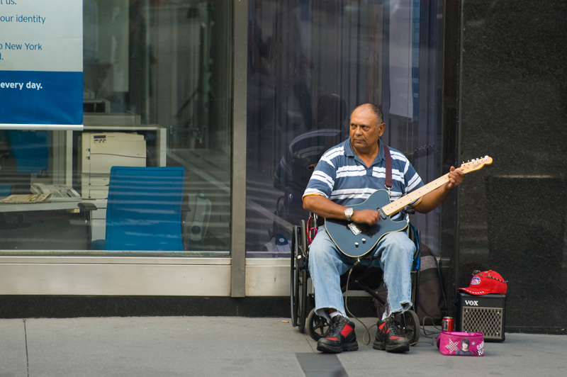 A man in a wheelchair plays an electric guitar for passers-by with money to spare.