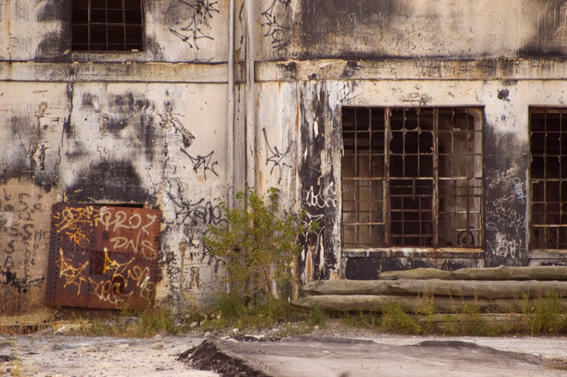 The exterior of a building shows many signs of deacy: rust, graffiti, and broken glass.