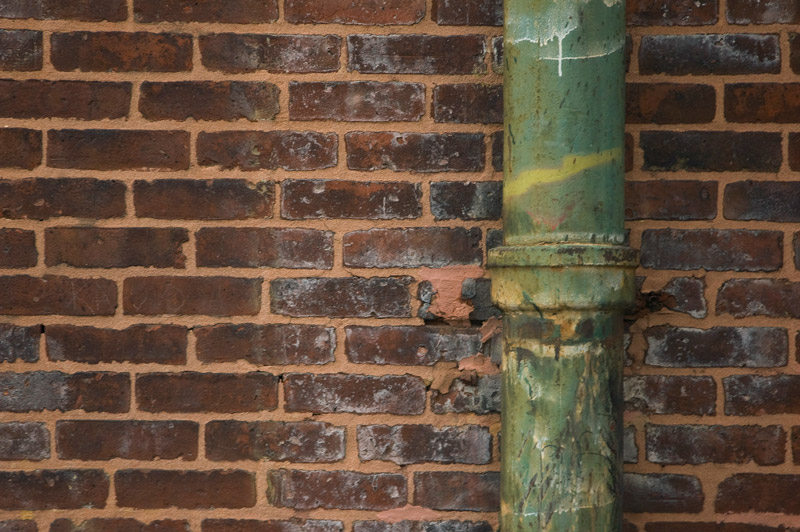 A green pipe is flush up against a red brick wall.