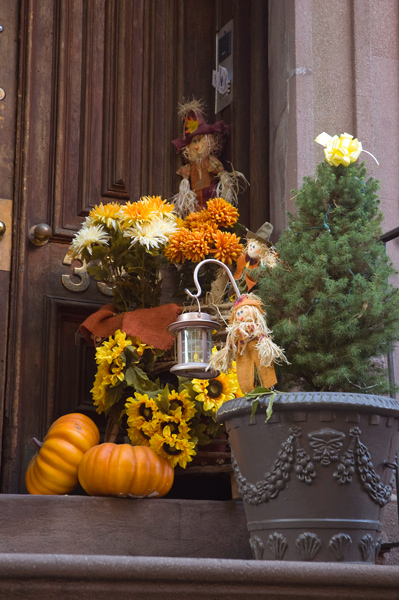 Pumpkins, small scarecrows, and orange carnations decorate a stoop.