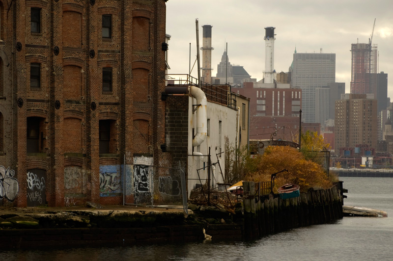 An old brick building covered with graffiti sits next to a waterway adjoining a river.