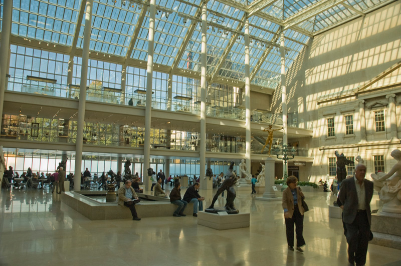 People stroll through a sunlit atrium with sculptures.