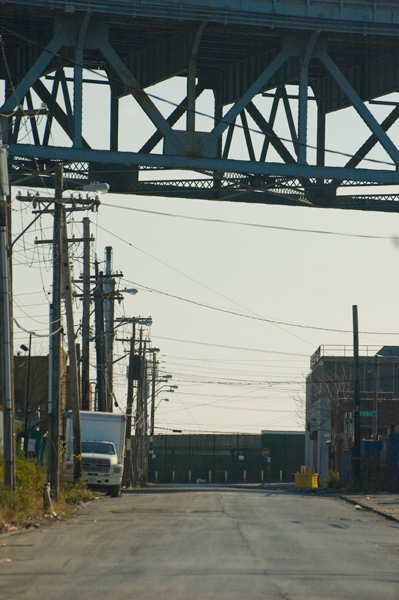An empty industrial street runs under the overpass of an expressway.