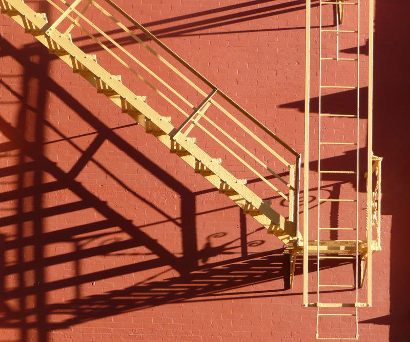A yellow fire escape casts detailed shadows on a red brick wall.