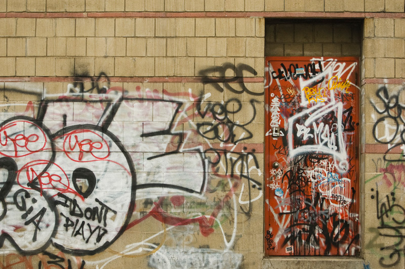Both a red door and its surrounding wall are covered in graffiti.