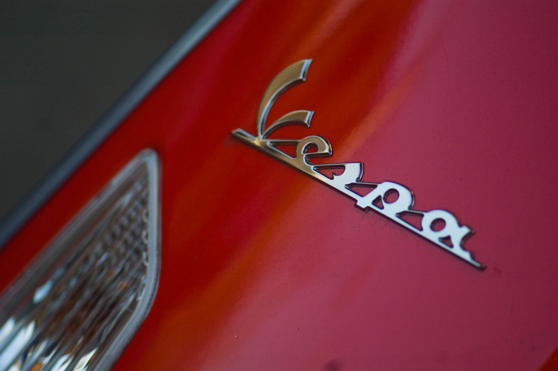 A Vespa motorcycle's chrome logo on a red motorcycle.