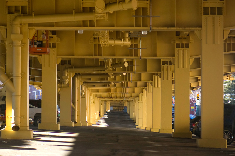 A series of yellow metal arches underneath a highway.