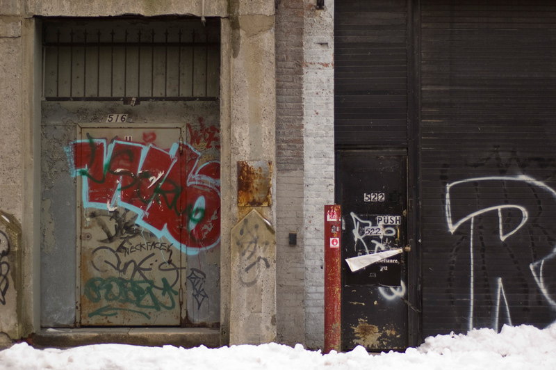 Two doors on industrial buildings, painted with bold graffiti.