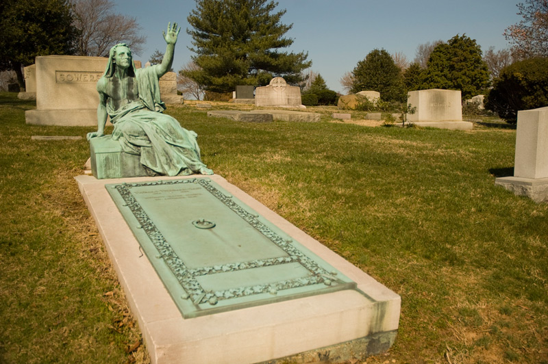 At a grave, a reclining robed statue raises its arm to the sky.