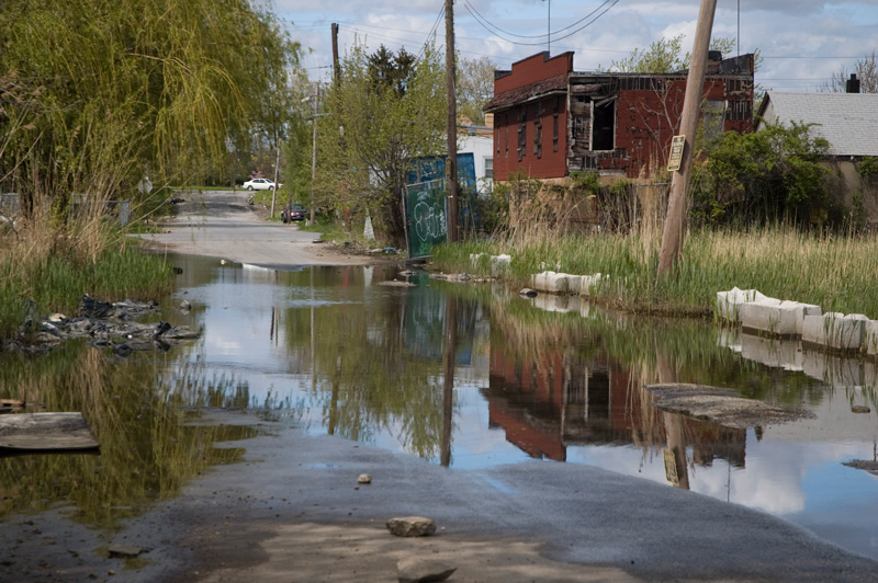 Water has settled in a street, with empty lots and abandoned buildings.