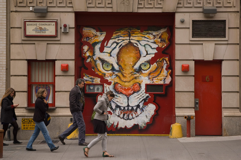 People walk past a fire house, painted with a tiger's face.