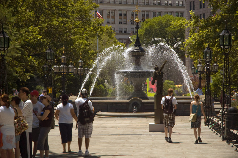 A sunny day, a water fountain in a plaza, and tourists.