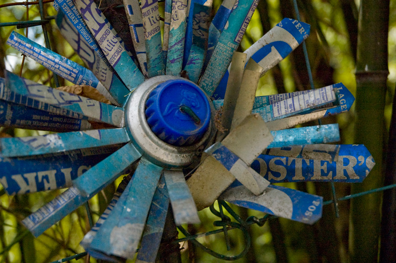 A metal flower wired to a fence, cut from a can of Foster's, Hawaiian Punch, and Nesquik packaging.