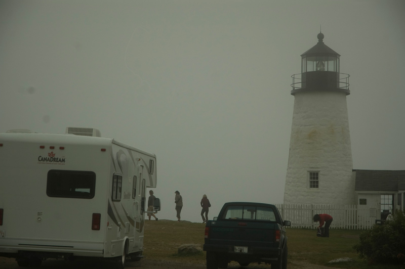 Tourists around a lighthouse; surrounded by fog.