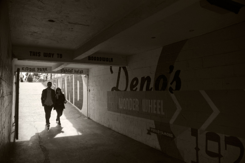 A couple strolls, arm in arm, into a dark underpass.