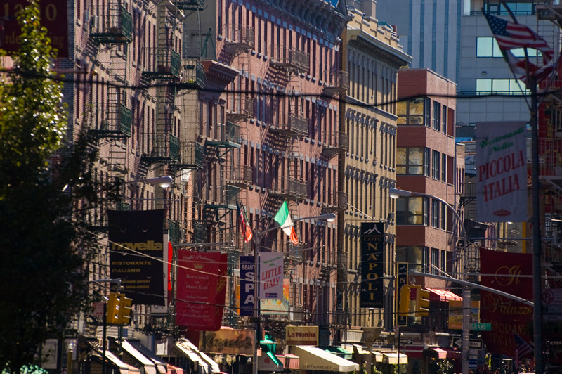 Rows of tall tenements with fire escapes, and Italian flags.