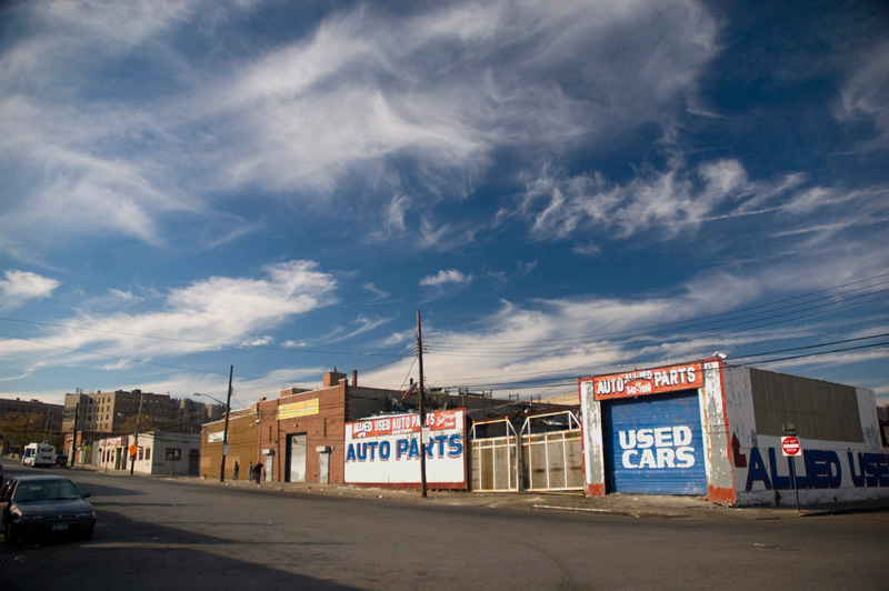 Blue skies and wispy clouds over a block with a seller of auto parts and used cars.