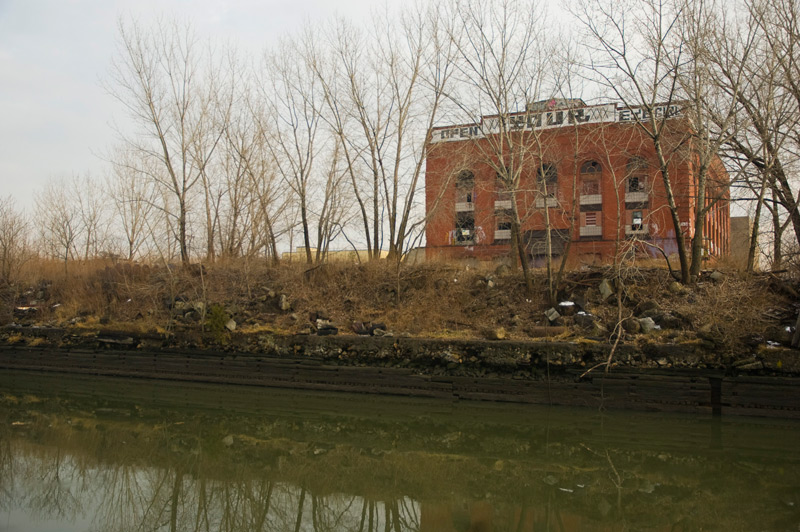 An abandoned building by the Gowanus Canal, with the words 'Open Your Eyes, Girl' painted at its top.