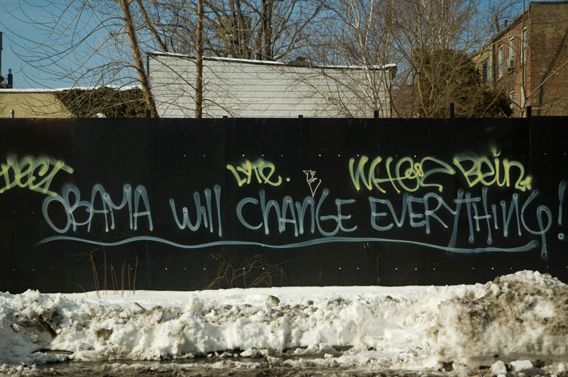 A black fence, spraypainted with 'Obama Will Change Everything!' in graffiti.