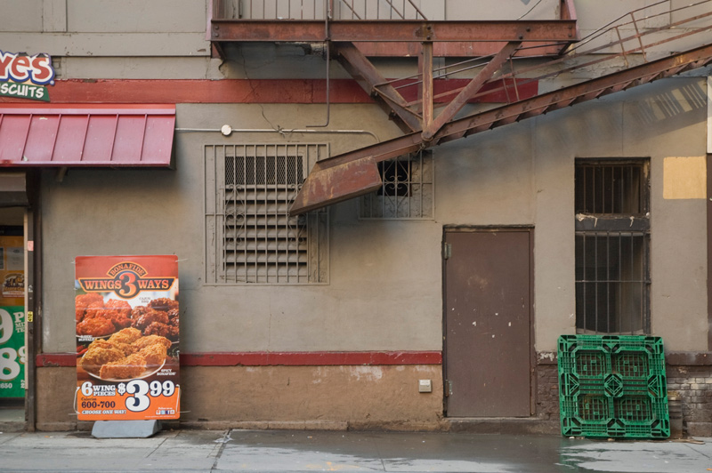 A sign advertising chicken wings, next to vents, a steel door, and a plastic palate.