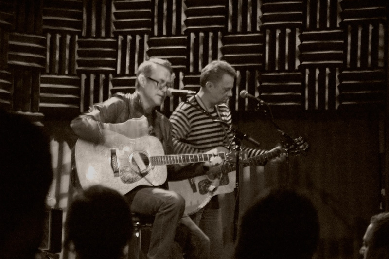 Two musicians with acoustic guitars on stage