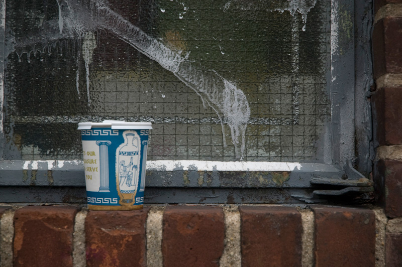 A blue paper coffee cup with Greek designs, resting on a brick window sill.